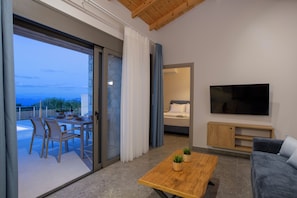 A modern living room with a sofa, a coffee table, a TV, and a balcony with a dining area. - Ionian Harmony Villa 1 | Private Pool & Sea View (Tsoukalades)