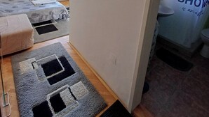 Una camera compatta con un letto, un piccolo angolo relax, un appendiabiti e un bagno visibile attraverso una porta aperta.