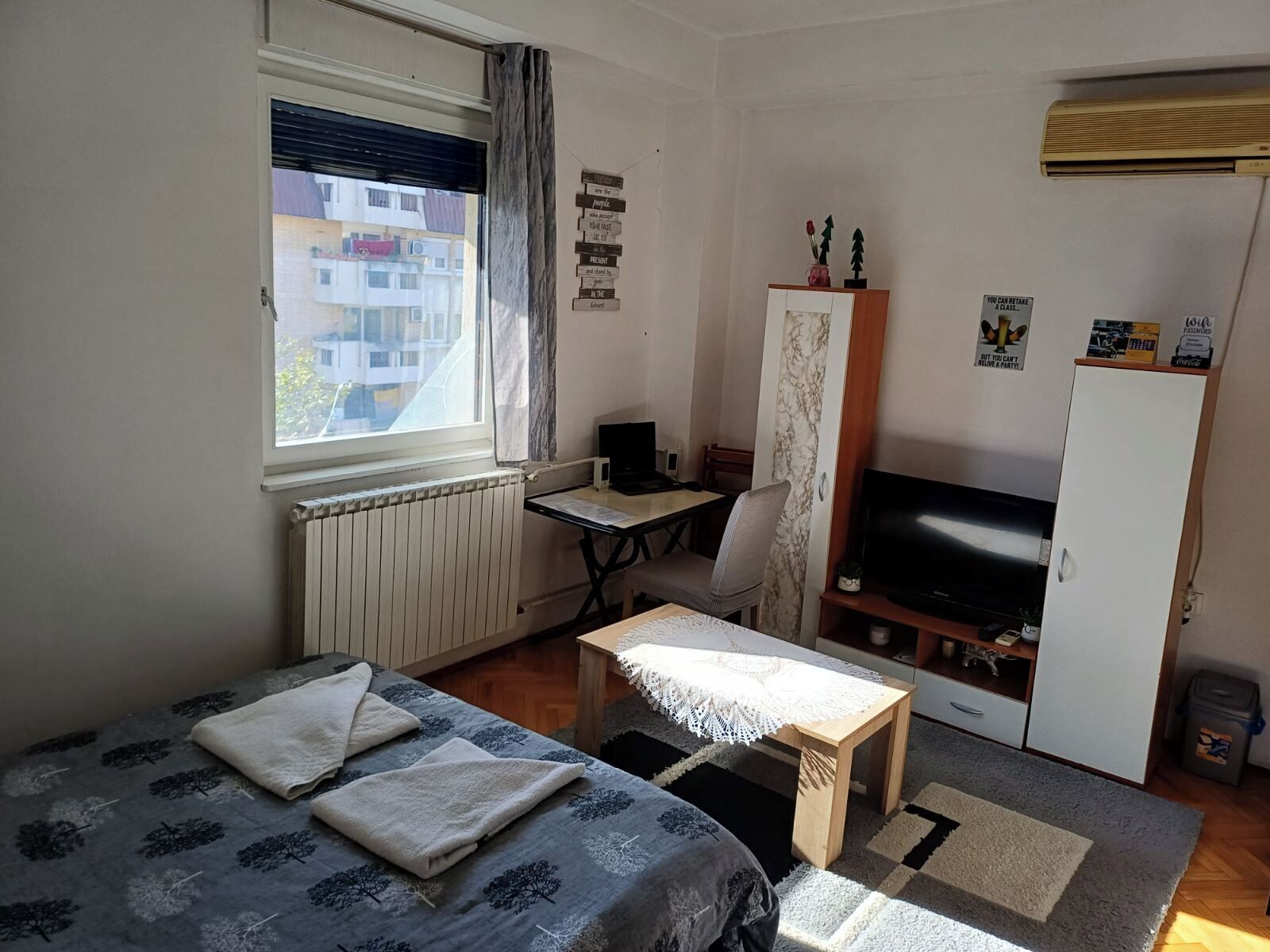 Een ruime, goed verlichte kamer met een bed, een bureau, een stoel, een televisie en een kledingkast.