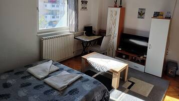 Een ruime, goed verlichte kamer met een bed, een bureau, een stoel, een televisie en een kledingkast.
