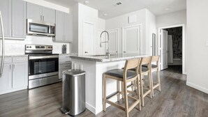 Una cucina moderna con elettrodomestici in acciaio inossidabile, un piano di lavoro in granito e un'area bar con sedie in legno.