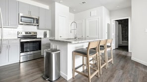 Eine moderne Küche mit Edelstahlgeräten, einer Granitarbeitsplatte und einer Bar mit Holzstühlen.
