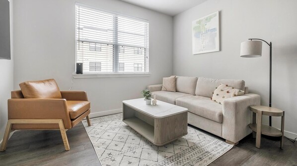 Een moderne woonkamer met een leren fauteuil, een beige bank, een salontafel en een vloerlamp.