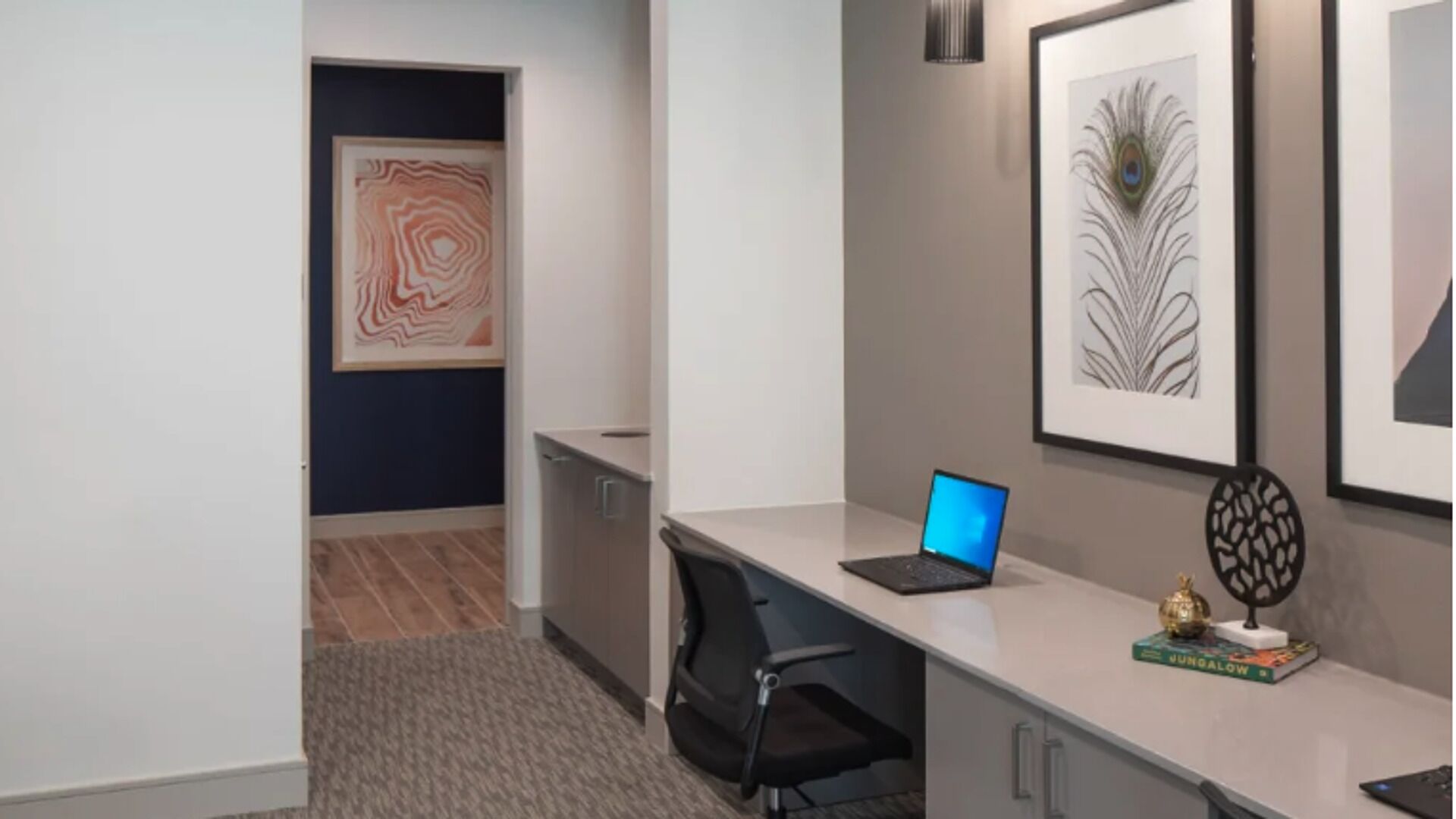 Ein moderner Arbeitsplatz mit Schreibtisch, Stuhl, Laptop und gerahmten Kunstwerken an der Wand.