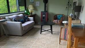 A living room with a sofa, a table, chairs, a fireplace, and a view through large windows. - Quiet apartment very close to Fontenay Abbey (Marmagne)