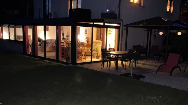 A house with a glass-enclosed patio area, a dining table, and chairs. - Quiet apartment very close to Fontenay Abbey (Marmagne)