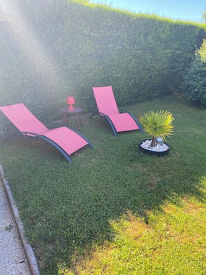 Un jardín con dos sillones rojos y una mesita con una lámpara.