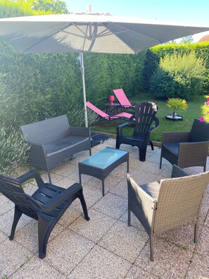 Une terrasse extérieure aménagée avec des meubles en osier, une table à plateau en verre et un grand parasol.