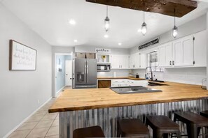 A modern kitchen with white cabinets, a wooden island, and hanging pendant lights.