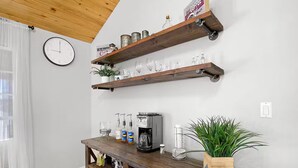 A room with wooden shelves holding glassware, a coffee machine, and a clock on the wall. - The Cozy Escape (Los Lunas)