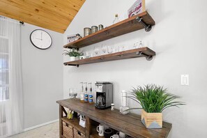 A room with wooden shelves holding glassware, a coffee machine, and a clock on the wall.
