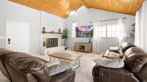 A living room with a fireplace, leather sofas, a coffee table, and a large TV. - The Cozy Escape (Los Lunas)