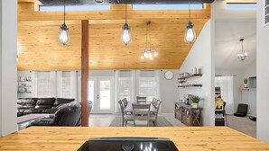 A modern kitchen with a central island, wooden ceiling, pendant lights, and a dining area with a table and chairs. - The Cozy Escape (Los Lunas)