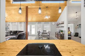 A modern kitchen with a central island, wooden ceiling, pendant lights, and a dining area with a table and chairs.