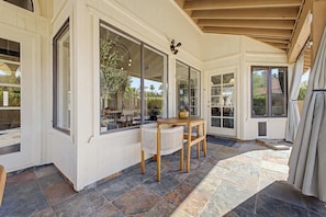 A covered patio with a table and chairs, large windows, and a stone floor. - NEW| Royal Palms Retreat | Pool, Spa & Pool Table (Tempe)