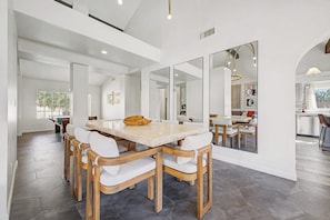 A spacious dining area with a large table and chairs, a kitchen in the background, and a large mirror reflecting the room. - NEW| Royal Palms Retreat | Pool, Spa & Pool Table (Tempe)