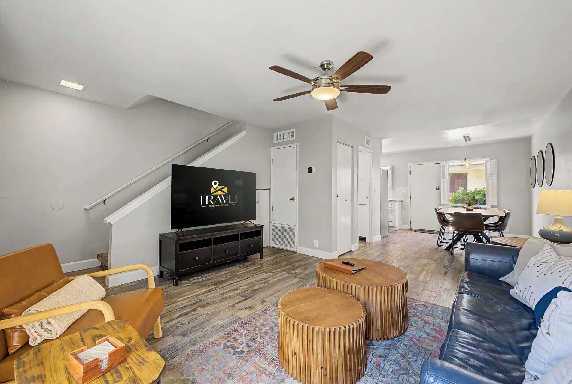 A modern living room with a flat-screen TV, wooden coffee table, leather sofa, and a dining area with a table and chairs.