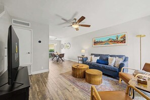 Ein Wohnzimmer mit Fernseher, Deckenventilator, Sofa, Couchtisch und einem Bild an der Wand.