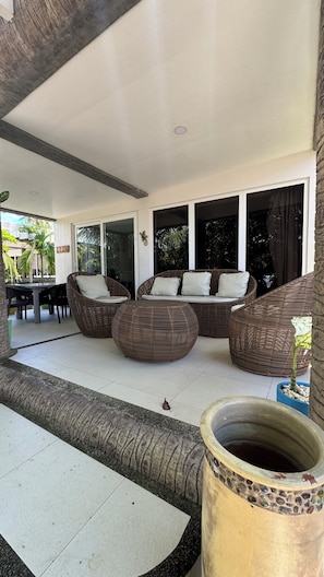 A covered outdoor seating area with wicker furniture, a dining table, and a decorative planter.
