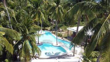 Piscina com a palavra 'PILI' na água, cercada por palmeiras e um edifício com telhado branco.