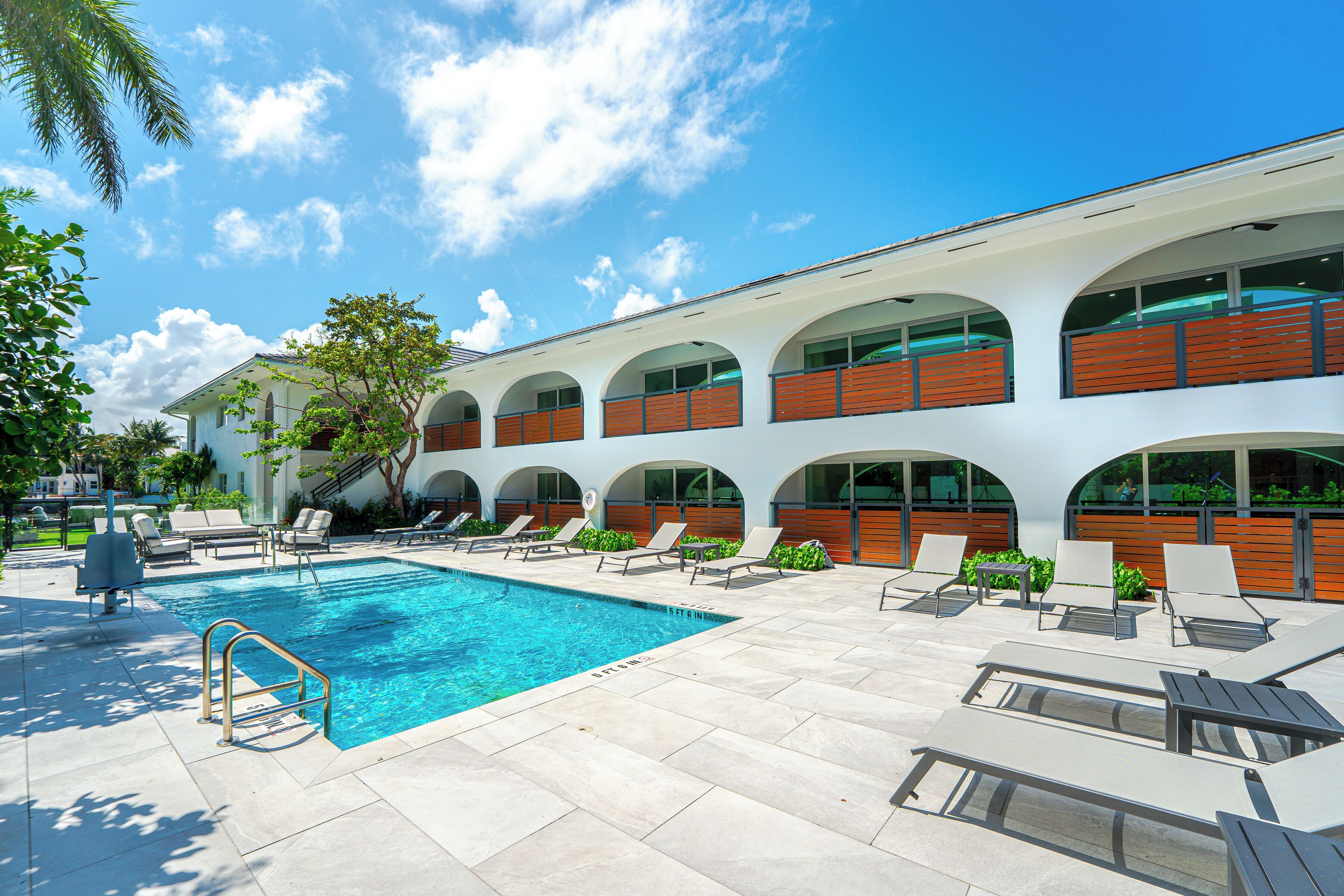 Una piscina con sillas de descanso, una escalera y un edificio con ventanas arqueadas.