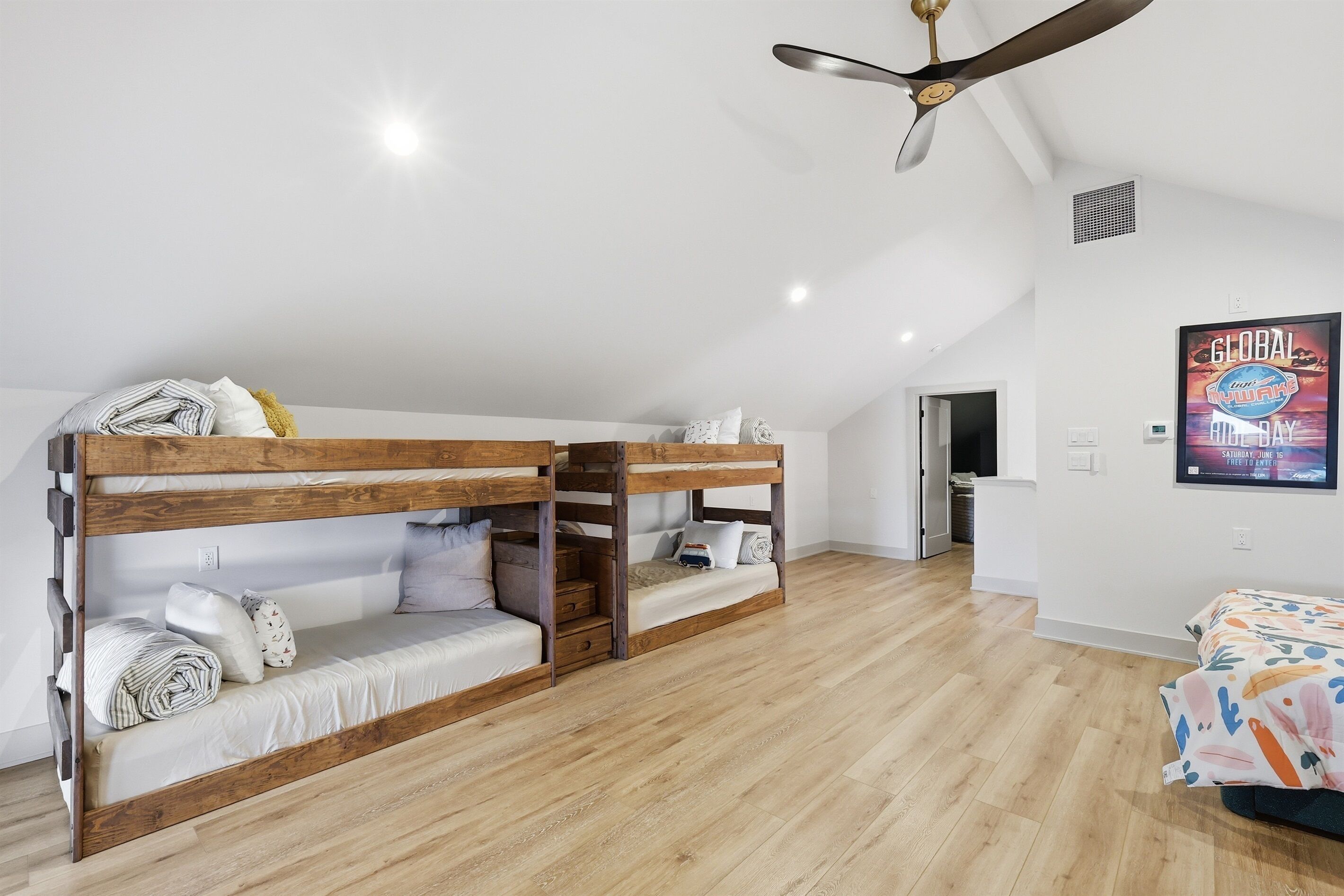 A bunk bed room with a ceiling fan, wooden flooring, and a poster on the wall.