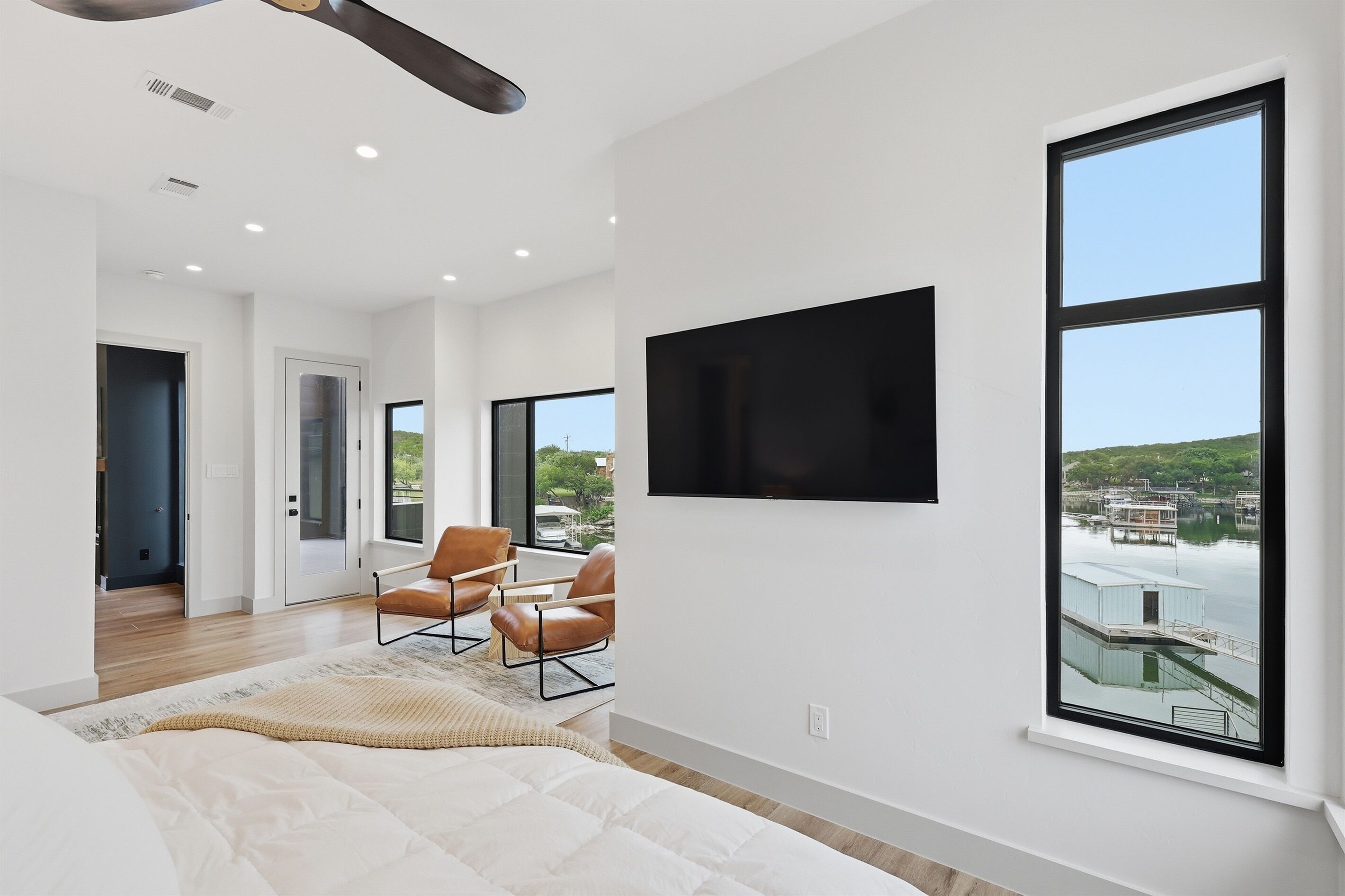 A modern bedroom with a large bed, a TV mounted on the wall, and a view of a dock and water.