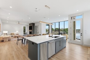 A modern kitchen with a large island, a dining area with a table and chairs, and a view of a body of water through large windows.