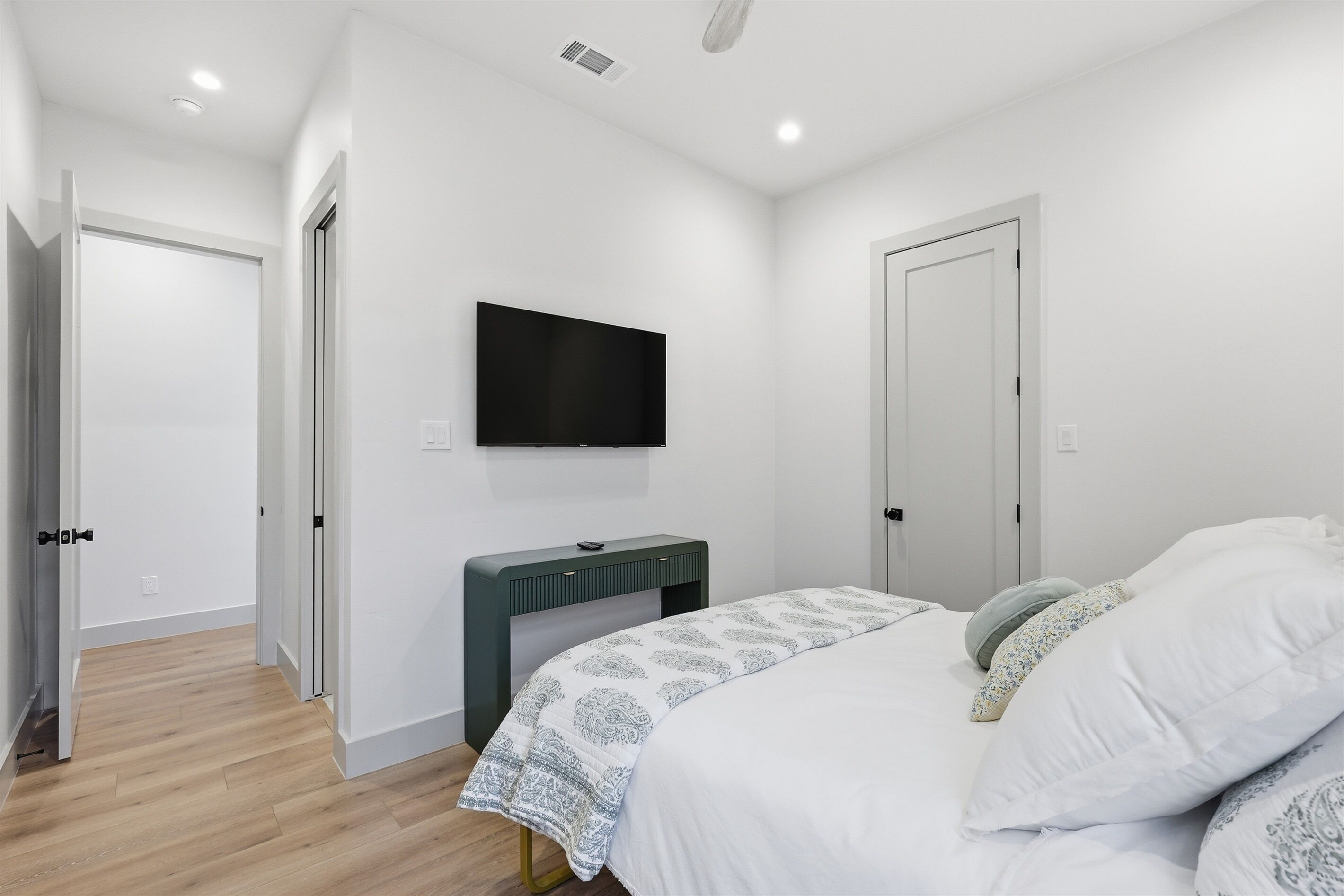 A bedroom with a bed, a flat-screen TV mounted on the wall, a bedside table, and a door.