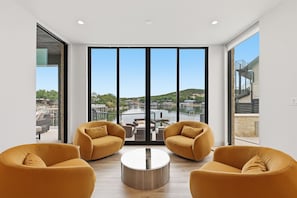 A modern room with large windows, two yellow sofas, a central coffee table, and a view of a water body and hills.