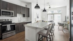 A modern kitchen with dark cabinets, stainless steel appliances, and a central island with bar stools. - Landing | Spectacular 1BD, Gym, Pool (Austin)