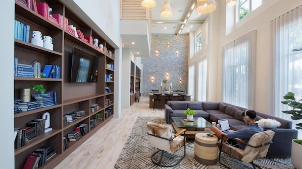 A spacious living area with a large bookshelf, a comfortable sofa, a coffee table, and a dining area with a stone wall. - Landing | Spectacular 1BD, Gym, Pool (Austin)