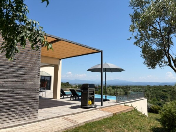 Eine moderne Terrassenanlage im Freien mit Pool, Liegestühlen und Grill.