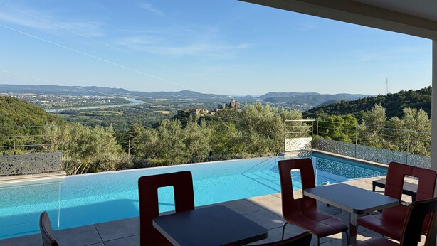 Piscina com mesa e cadeiras, vista para um vale e céu claro.