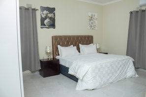 A bedroom with a large bed, a nightstand, a lamp, and two wall-mounted paintings.