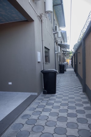 A narrow alleyway with patterned pavement, trash bins, and buildings with external air conditioning units.