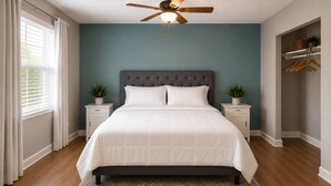 Une chambre à coucher avec un lit, deux tables de chevet, un ventilateur de plafond et une fenêtre avec des rideaux.