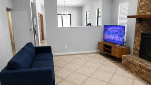 Un salon avec un canapé bleu foncé, un téléviseur posé sur un meuble en bois, un tapis beige et une cheminée en briques.