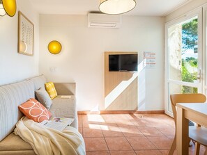 A modern living room with a sofa, a television, a dining table, and a staircase leading to an upper level. - Riverside Apartment Near Cannes (Mandelieu-La-Napoule)