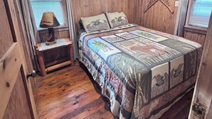 A wooden-paneled room with a bed, a nightstand, and a window with blinds.
