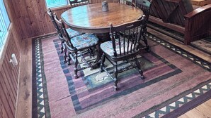 A wooden interior with a round table and chairs, a sofa, and a patterned rug.