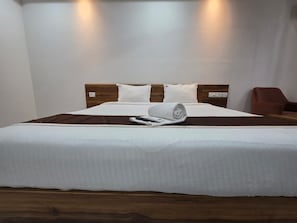 Una cama bien hecha con cabecera de madera, una colcha blanca y una toalla enrollada.