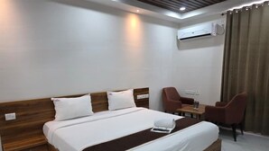 A hotel room with a wooden bed, white bedding, a small table with chairs, and an air conditioning unit on the wall. - Varsha Grand  (Hyderabad)