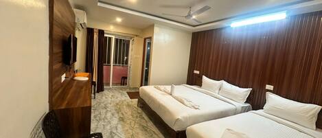 A hotel room with two beds, a TV, a desk, and a bathroom with a shower.