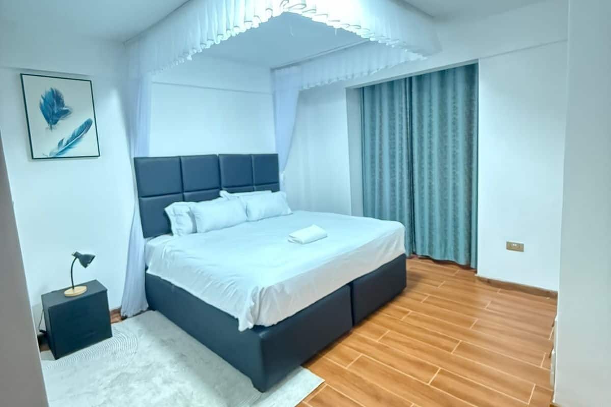 Un dormitorio moderno con una cama grande, una mesita de noche, una lámpara de pared y un cuadro enmarcado.