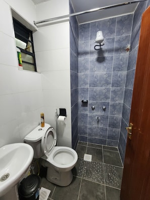 Un baño con inodoro, lavamanos, ducha y una pequeña ventana.