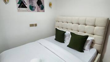A neatly made bed with a white duvet, green and white pillows, and a rolled white towel.