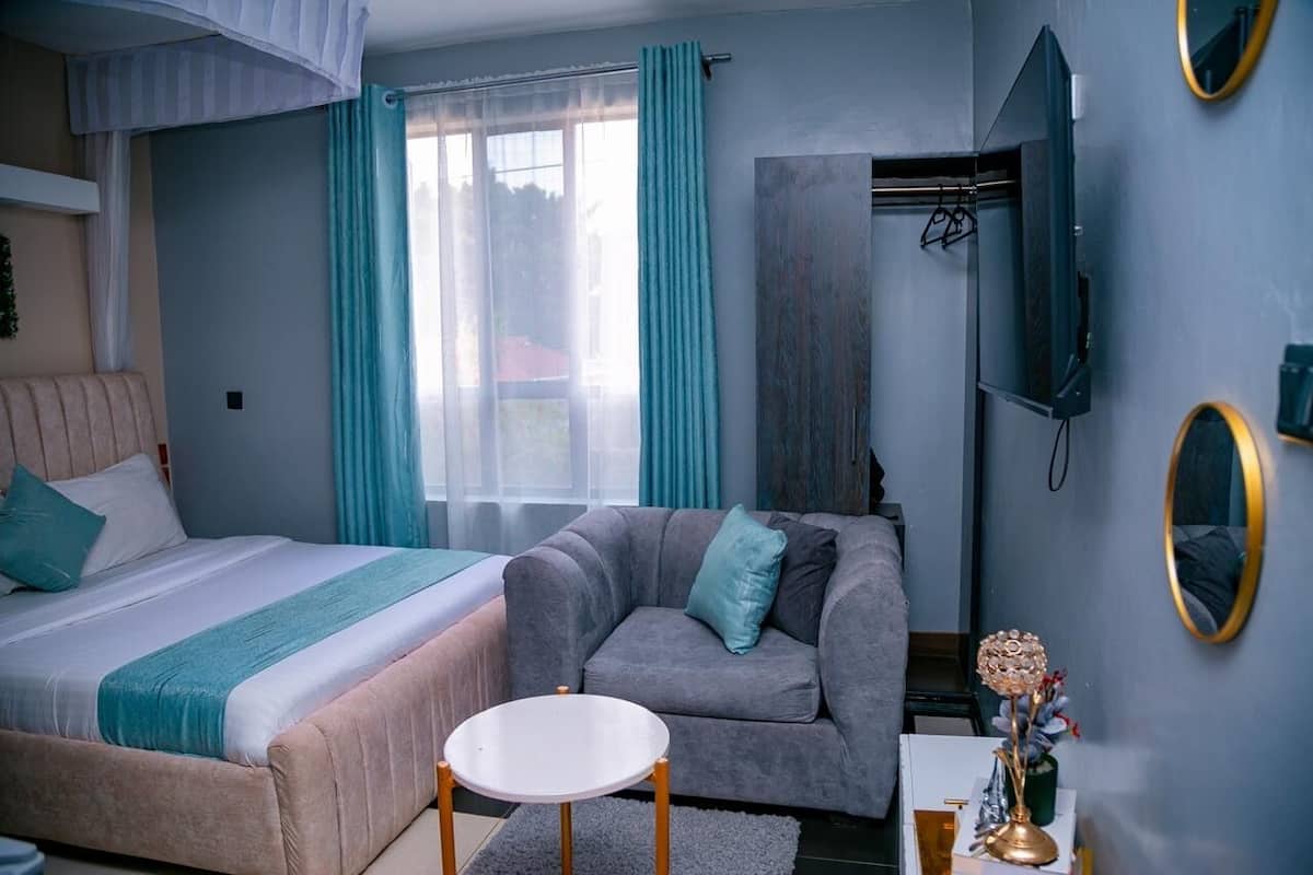 Un dormitorio con cama, sofá gris, una mesita redonda y televisor montado en la pared.