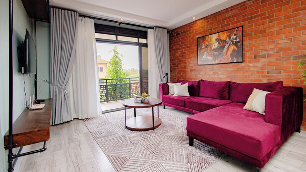 A modern living room with a red sofa, a flat-screen TV, a round coffee table, and a patterned rug. - Rustic, quiet and cozy 1-bedroom condo with fantastic views. (Kampala)