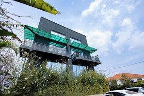 Un edificio moderno con balcones, rodeado de vegetación bajo un cielo despejado.
